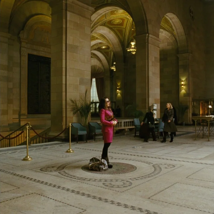 Mommy (2014) movie still: fullbody — A spacious museum hall with high vaulted ceilings and intricate stone flooring patterns. A woman in a pink suit…