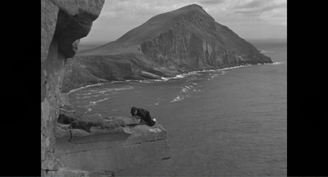 Made in England: The Films of Powell and Pressburger (2024) movie still: wide — A rocky, jagged cliff face overlooks a vast body of water under a…