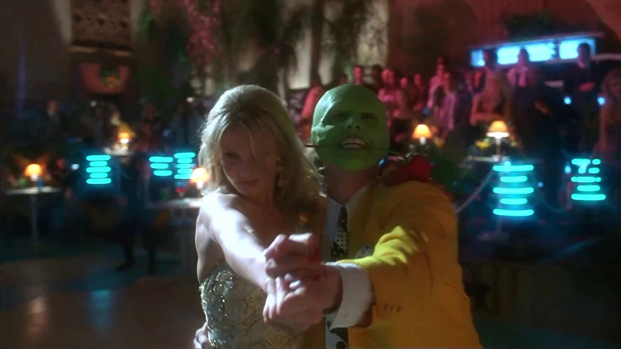 The Mask (1994) movie still: medium — A dimly lit nightclub features neon blue accent lights and tables with small lamps. A woman in a sequin dress…