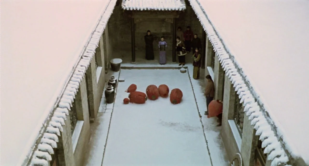 Raise The Red Lantern movie still: wide — A snow-covered courtyard of a traditional house is enclosed by symmetrical gray stone wings. Several…