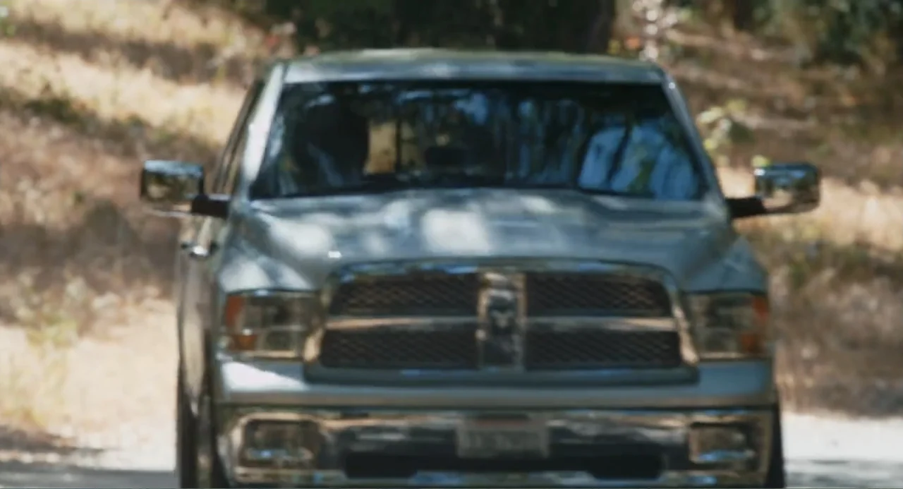 Gates of Darkness (2019) movie still: medium — A silver pickup truck drives along a dirt road lined with dry brush. The vehicle approaches the…