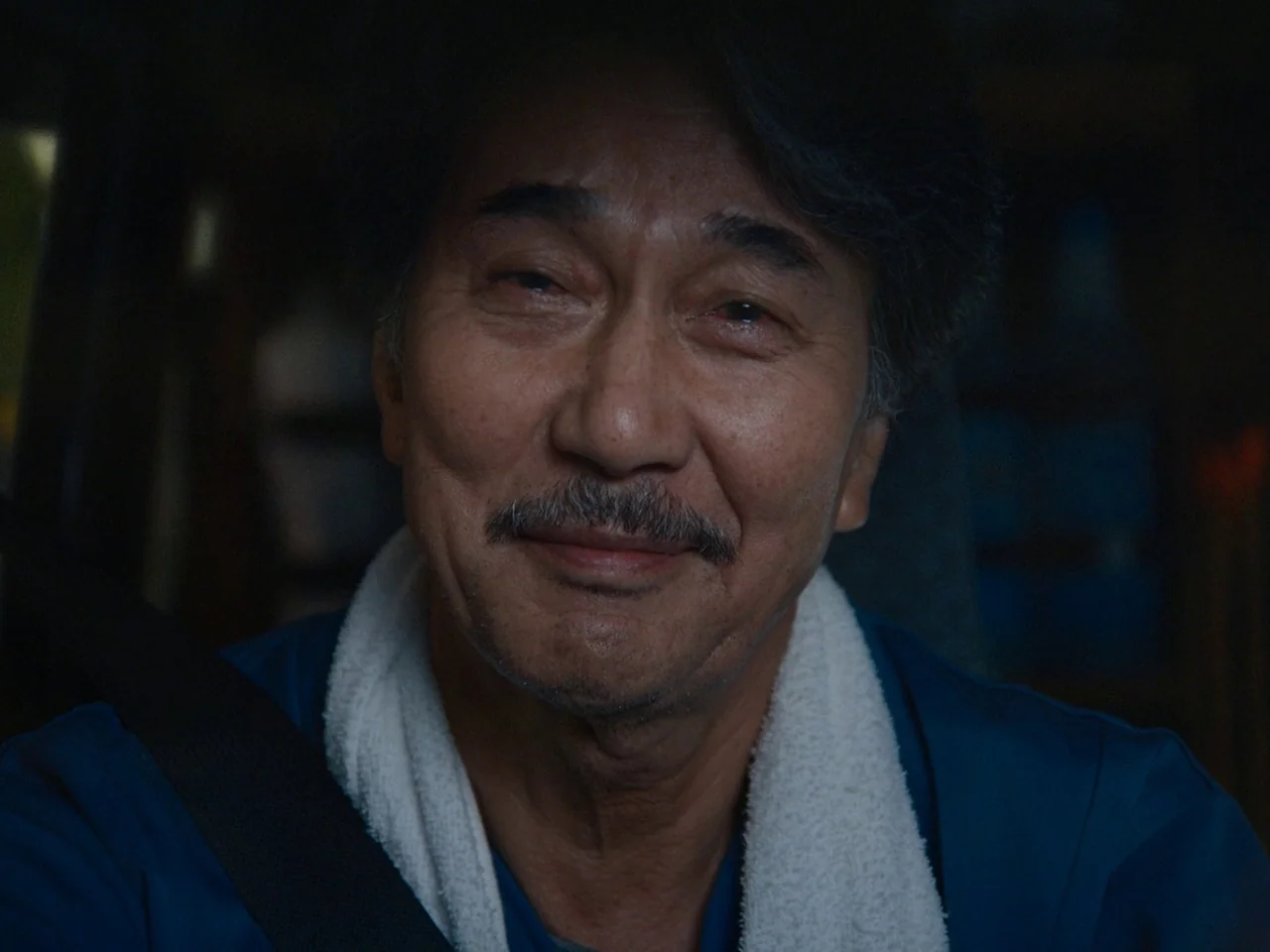 Perfect Days (2023) movie still: closeup — The interior of a vehicle at night with dark shadows obscuring the surroundings. An older man with a…