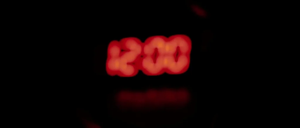 We Need To Talk About Kevin (2011) movie still: closeup — A digital alarm clock display glows red in complete darkness. The time is set to twelve…