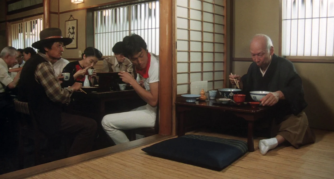 Tampopo (1985) movie still: wide — A traditional Japanese restaurant features wooden pillars, shoji screen dividers, and straw mats. Several patrons…
