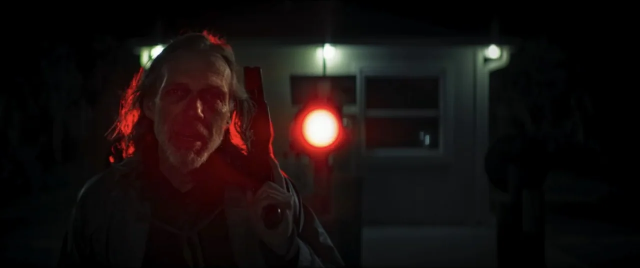 Offseason (2022) movie still: medium — A man stands outdoors at night near a small illuminated building with a dark parking lot. The man holds a…