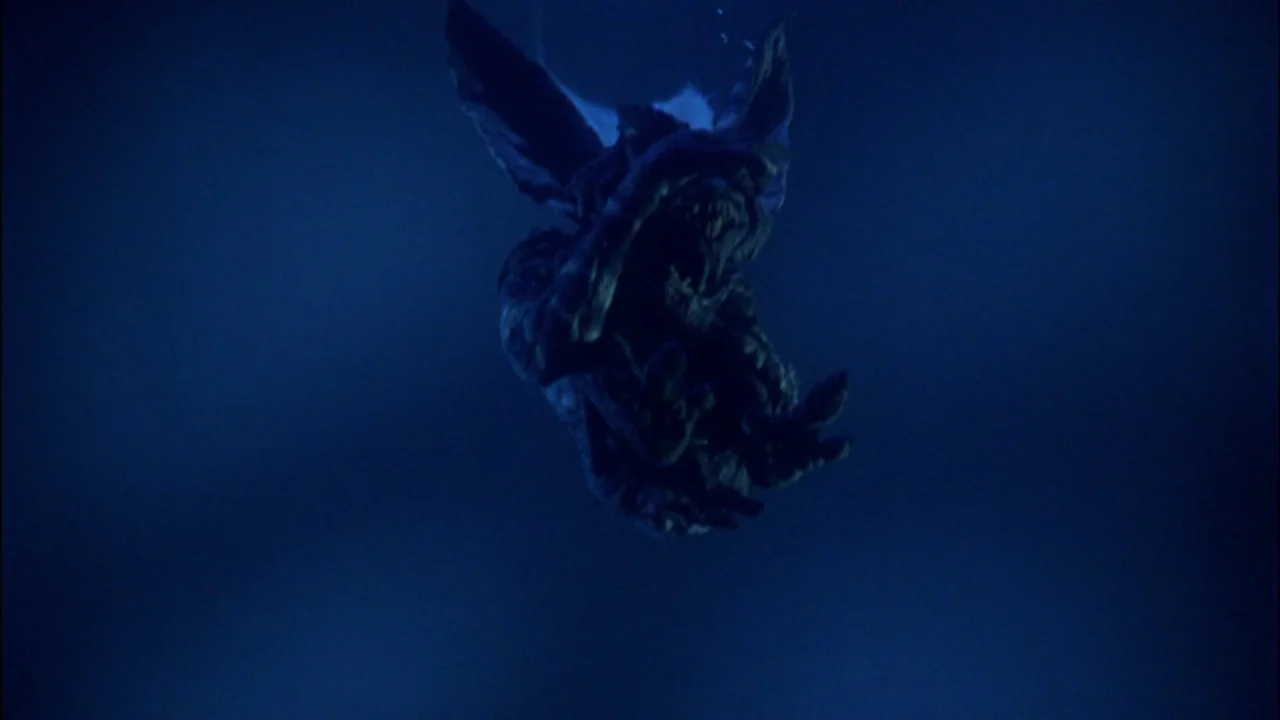 Gremlins (1984) movie still: medium — A dark, deep blue expanse of water with a creature sinking downward. The small monster descends with its mouth…