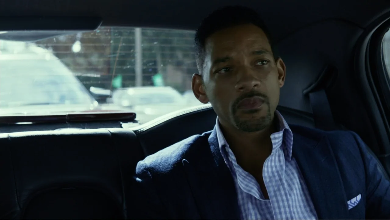 Focus (2015) movie still: medium — The interior of a moving vehicle with leather seats and visible rear window glass. A man sits in the backseat,…
