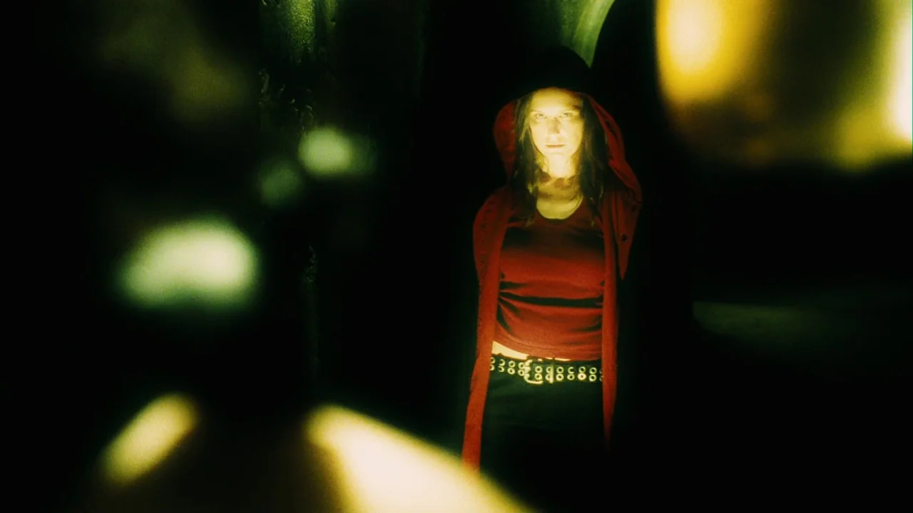 Saw III (2006) movie still: medium — A woman in a red hoodie stands in a nearly pitch-black environment. Light hits her face and torso while the…