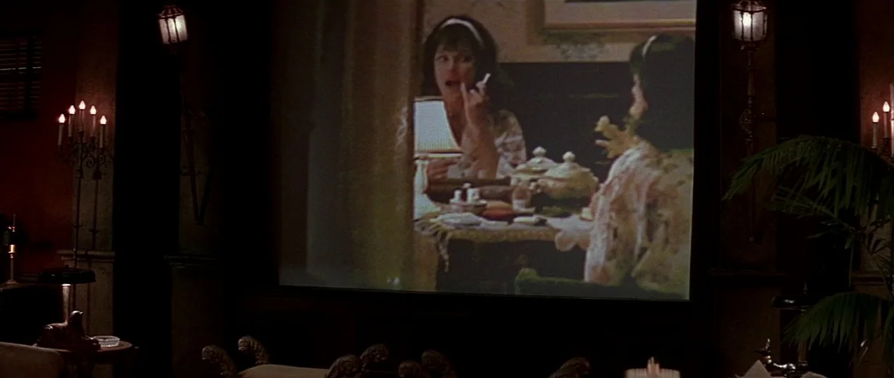 Scream 3 (2000) movie still: wide — A dimly lit home theater features a large projection screen showing a film scene. The interior includes ornate…