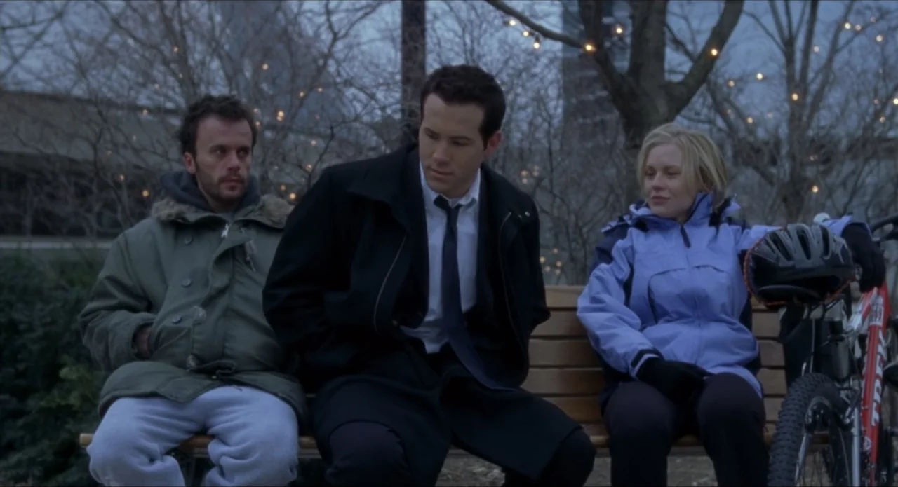 Foolproof (2003) movie still: medium — Three people sit on a wooden bench in a public park at dusk. The individuals remain seated while one holds a…