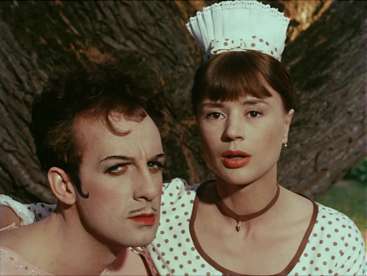 All These Women (1964) movie still: medium — A close outdoor shot shows two figures standing in front of a tree bark background. The woman wears a…