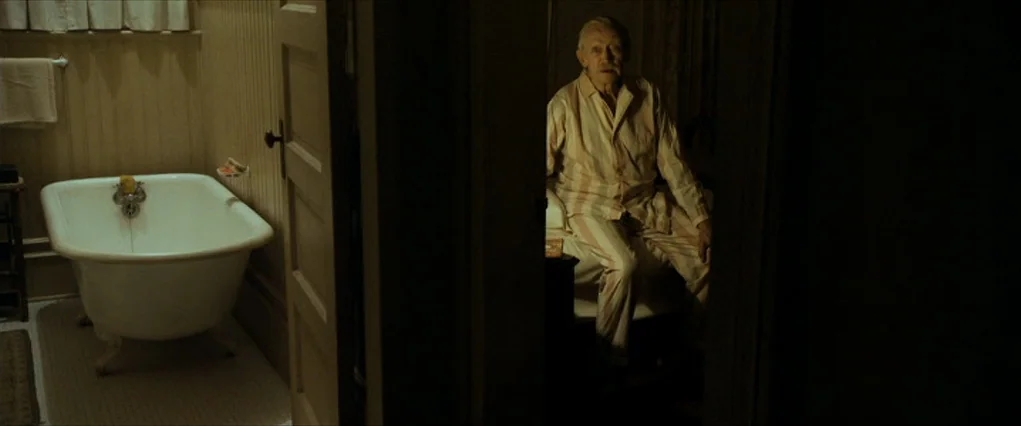 The Curious Case Of Benjamin Button (2008) movie still: wide — A partitioned space shows a white porcelain clawfoot tub in a tiled bathroom. Through…