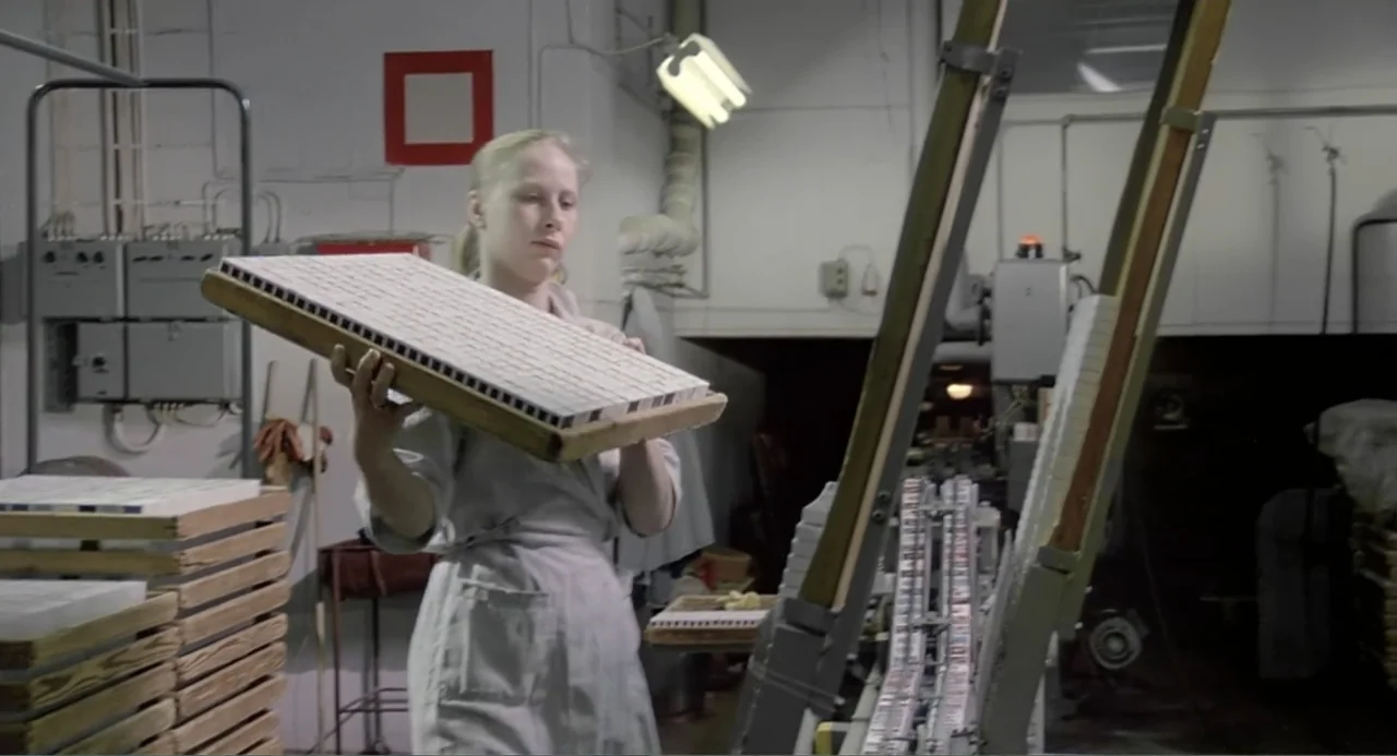 The Match Factory Girl (1990) movie still: medium — An industrial factory floor features heavy machinery and stacks of wooden material storage…