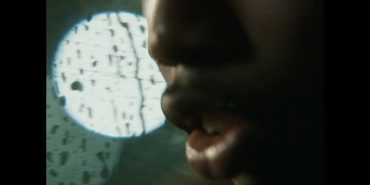Autumn Beat (2022) movie still: closeup — A close view of a person's mouth and jaw inside a dark vehicle. A bright circular light shines through a…
