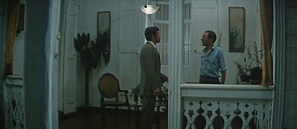 Mississippi Mermaid (1969) movie still: fullbody — A residential porch features white wooden railings and tall paneled shutters at night. One man in…