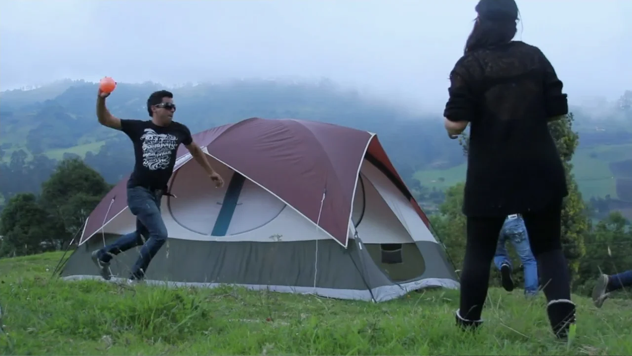 Aquel Septiembre (2018) movie still: fullbody — A grassy hill holds a large dome tent under a cloudy sky. A man in a black t-shirt prepares to throw…