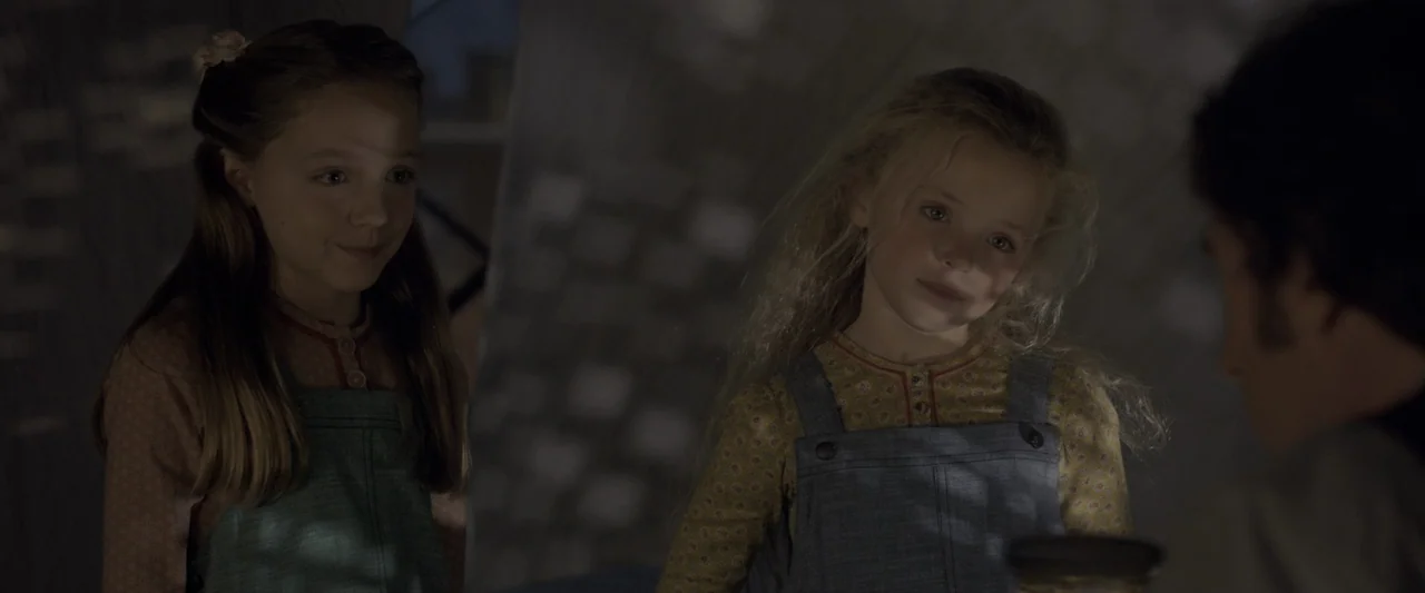 The Greatest Showman (2017) movie still: medium — Two young girls wearing overalls stand in a dark, indistinct room. They look towards an adult…