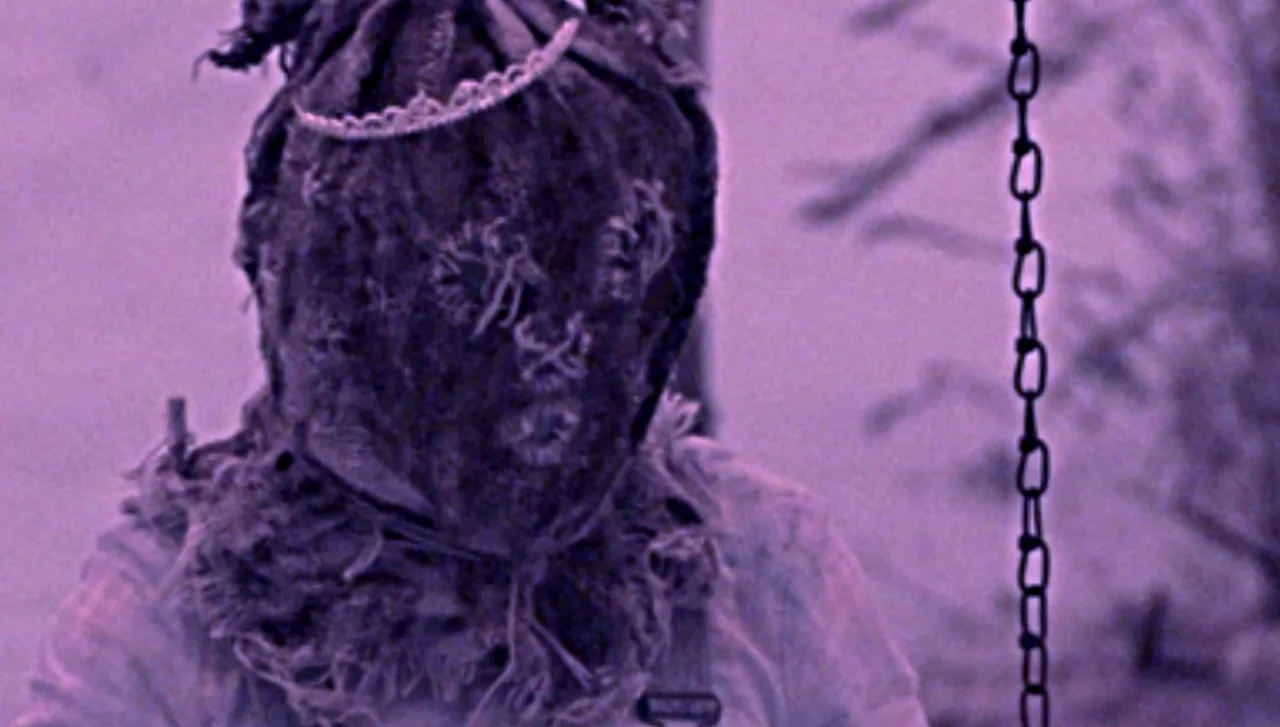 Hellions (2015) movie still: closeup — A close-up shot focuses on a figure wearing a handmade burlap mask with stitches. A small silver tiara is…