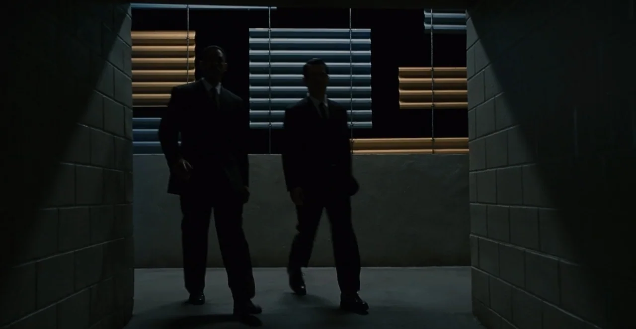Men in Black 3 (2012) movie still: fullbody — A dark concrete corridor with industrial horizontal panels visible in the background distance. Two men…