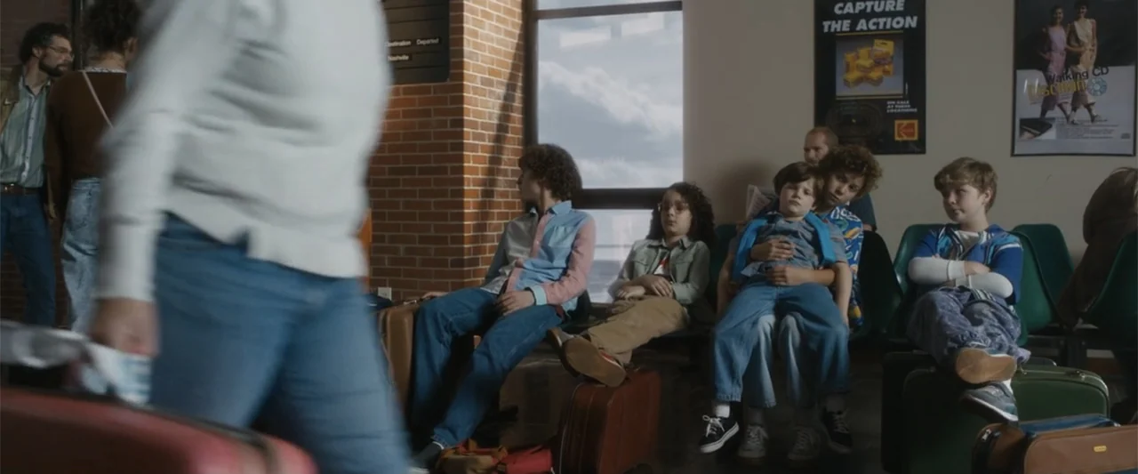 Unsung Hero (2024) movie still: medium — A terminal waiting area features brick pillars, green plastic chairs, and large windows. A group of…
