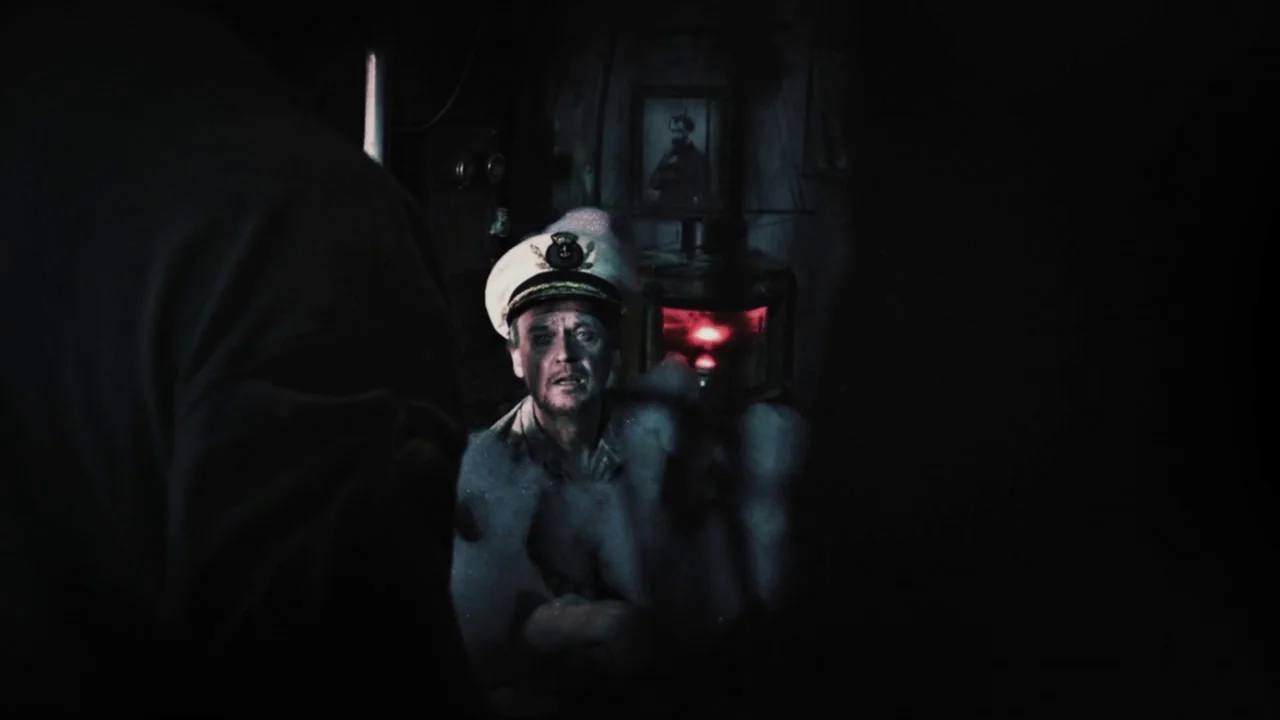 The Forbidden Room (2015) movie still: medium — A dark, cramped military cabin interior features pipes, wooden wall panels, and dim red lighting. A…