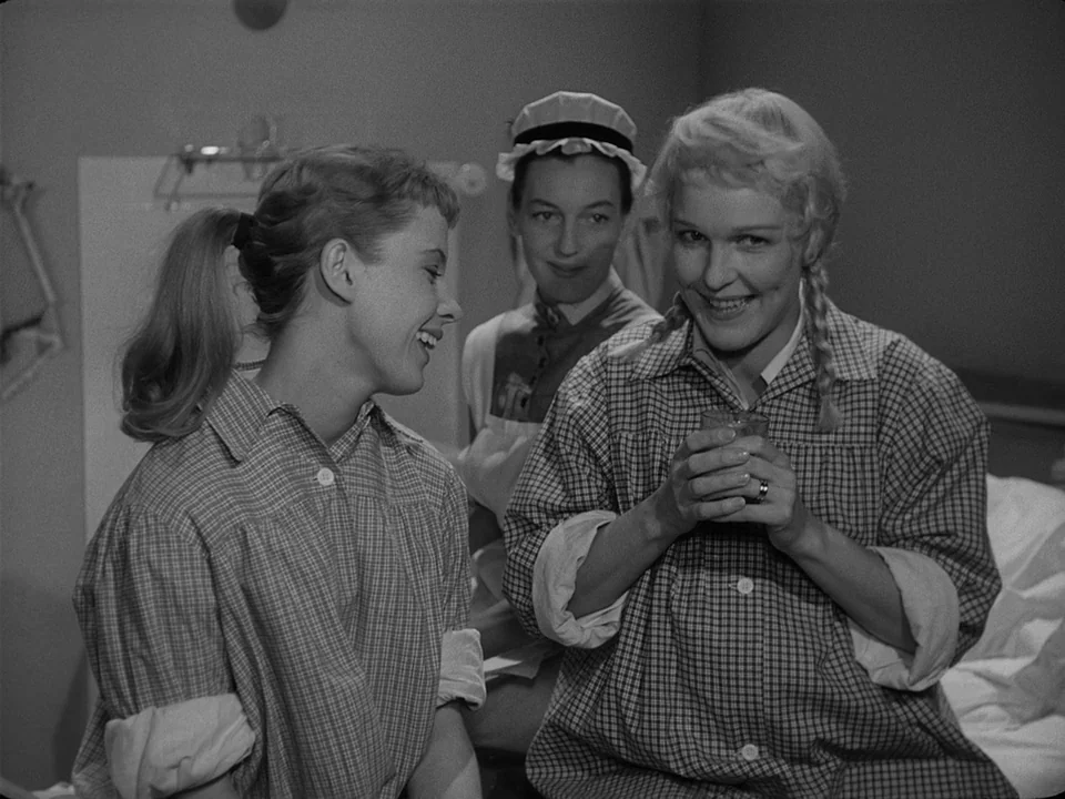 Brink of Life (1958) movie still: medium — A hospital interior featuring patients in plaid pajamas and a attending nurse. The blonde woman in the…