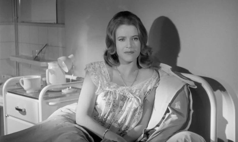 Eyes Without A Face (1960) movie still: medium — A hospital room features a simple white metal bedframe and a rolling medical trolley. A woman in a…