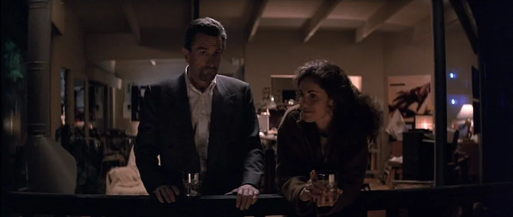 Heat (1995) movie still: medium — A dark apartment balcony at night overlooks a dimly lit interior living space. A man and a woman stand side by…
