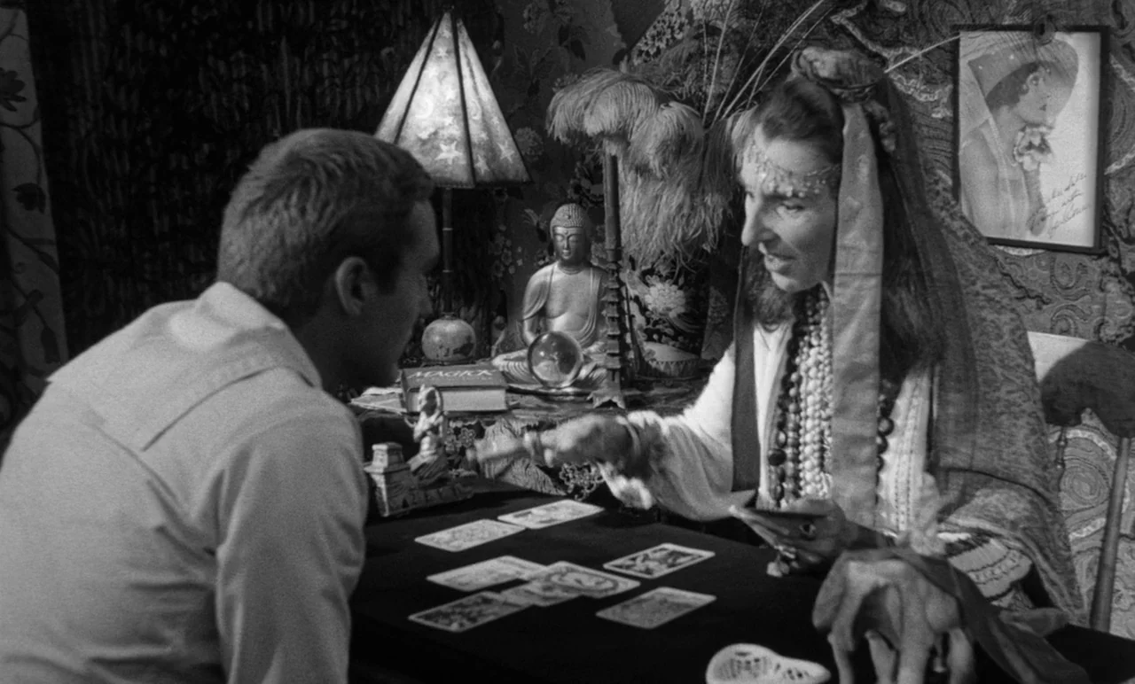 Night Tide (1961) movie still: medium — A crowded interior filled with esoteric objects like a Buddha statue and crystal ball. A woman gestures…