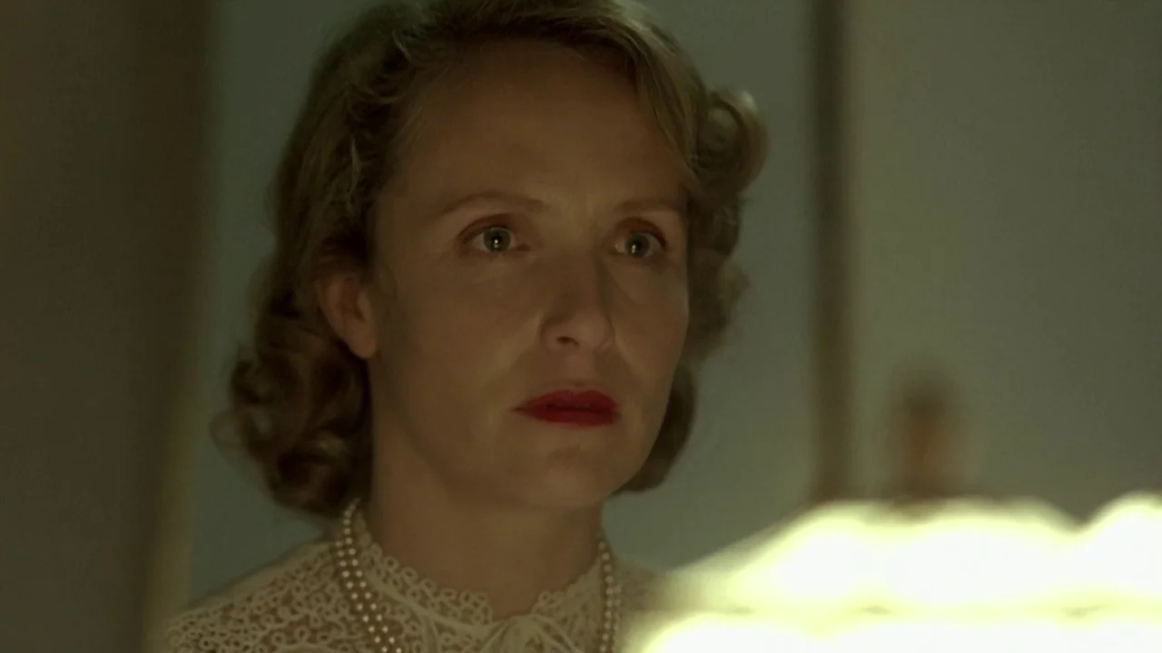 Downfall (2004) movie still: closeup — A woman's face is lit by the soft glow of a nearby lamp. She stands against a nondescript, dimly lit wall.