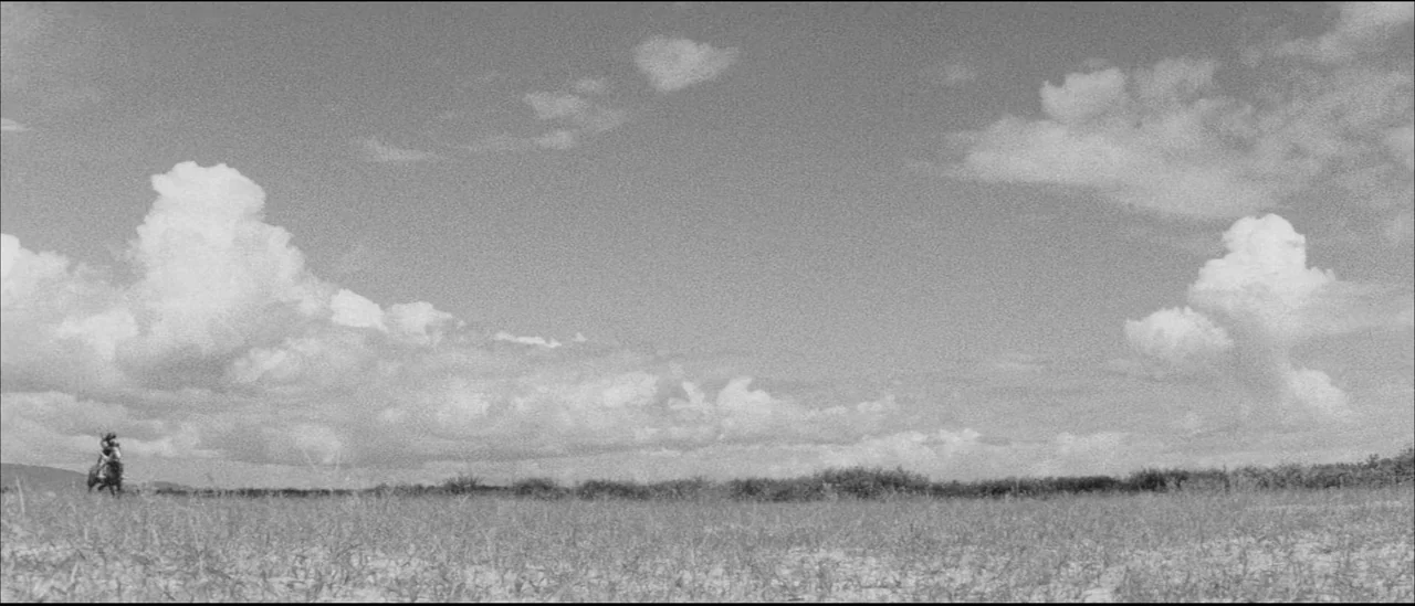 Kuroneko (1968) movie still: wide — A vast, flat prairie stretches toward a distant horizon under a large cloudy sky. A solitary rider on horseback…
