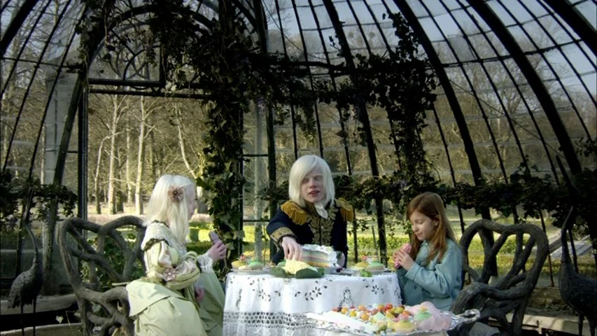 The Sleeping Beauty (2010) movie still: medium — A glass-domed greenhouse contains a small round table set with an array of pastries. Three people…