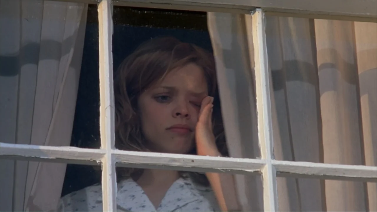 The Notebook (2004) movie still: closeup — A wooden window frame separates the viewer from a young woman inside. The woman rests her head on her…