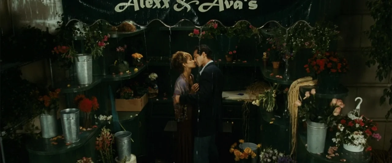 Catwoman (2004) movie still: medium — A flower shop interior features dark shelves filled with potted plants and metal buckets. A couple stands…