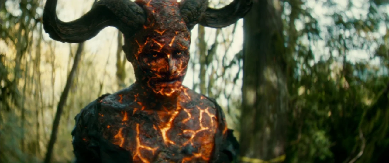 Horns (2013) movie still: medium — A dense patch of trees creates a shallow depth of field behind a demon. The demon character stands facing the…
