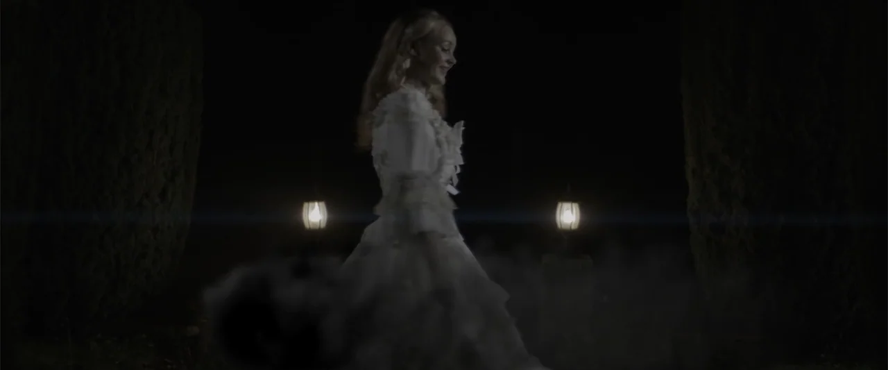 Cinderella's Curse (2024) movie still: fullbody — A woman in a white gown walks outdoors at night between dark trees. Two small lanterns glow on…
