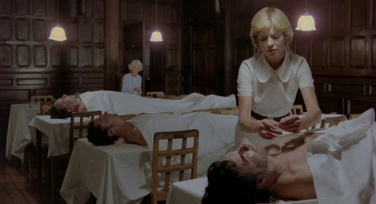 The Shout (1978) movie still: medium — A room with dark wood paneled walls contains several cots draped in white cloths. A woman in a white blouse…