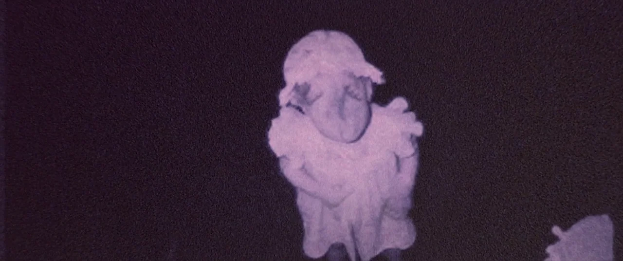 Skinamarink (2022) movie still: medium — A dark environment surrounds a single small figure captured in a grainy, low-light image. The child-sized…