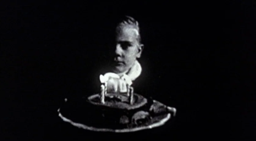 The Saddest Music in the World (2003) movie still: medium — A young boy sits in a pitch-black environment with no visible background. He watches the…