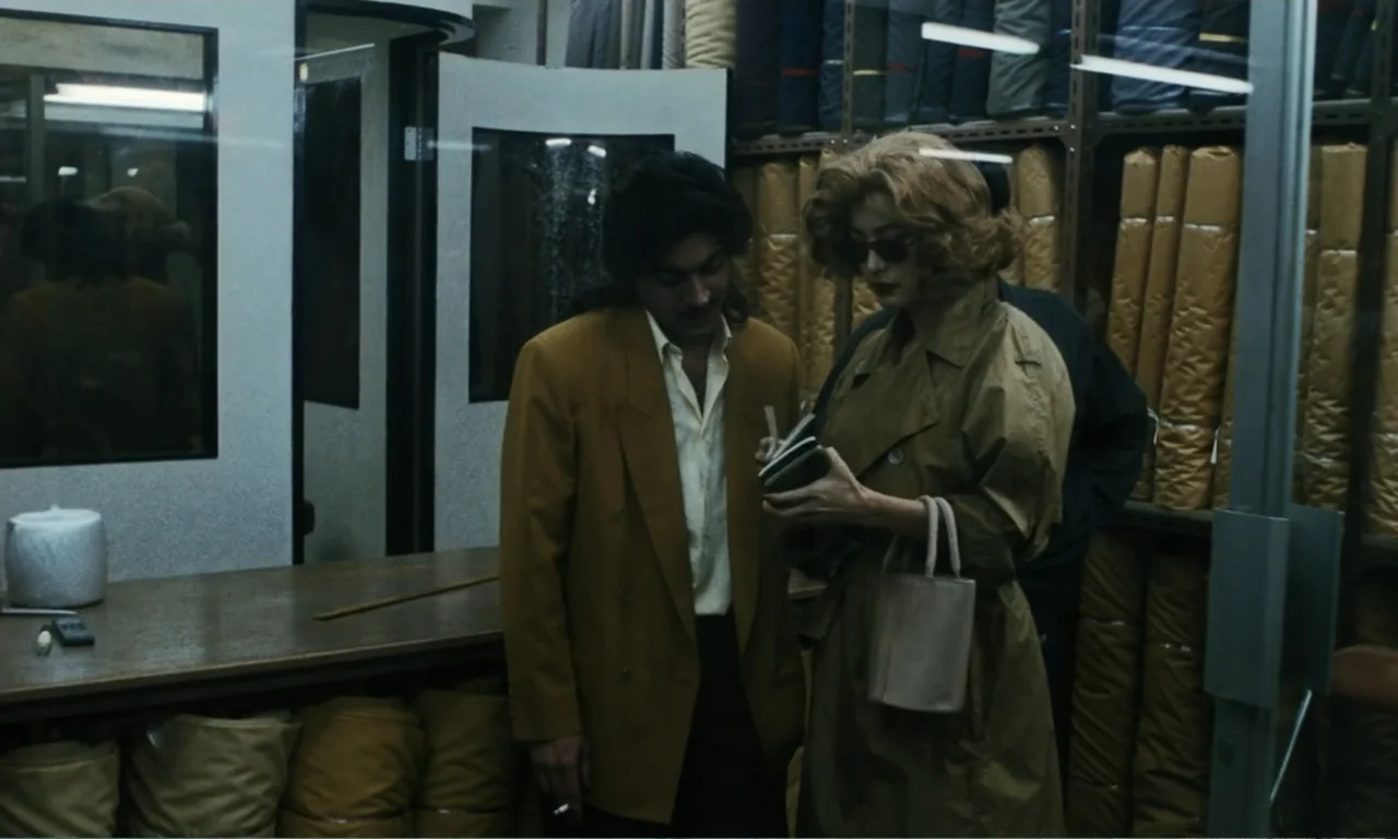 Chungking Express (1994) movie still: medium — A cluttered fabric shop features tall metal shelves packed with stacked textile bolts. A man and a…