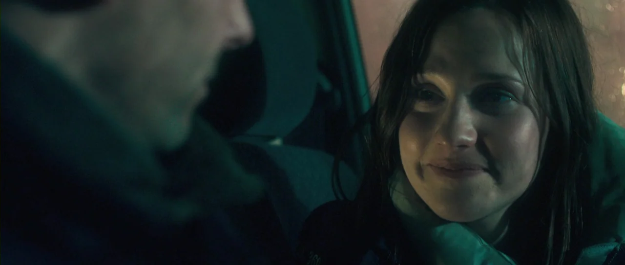 Grabbers (2012) movie still: closeup — The interior of a vehicle at night with green ambient lighting visible. A woman looks toward a man whose…