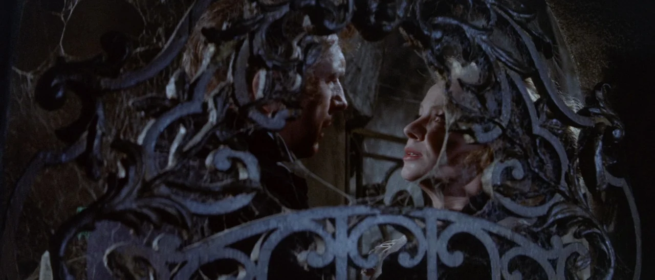 The Tomb of Ligeia (1964) movie still: medium — An ornate, dark wrought-iron gate obscures a dimly lit, cobweb-covered interior room. A man and a…