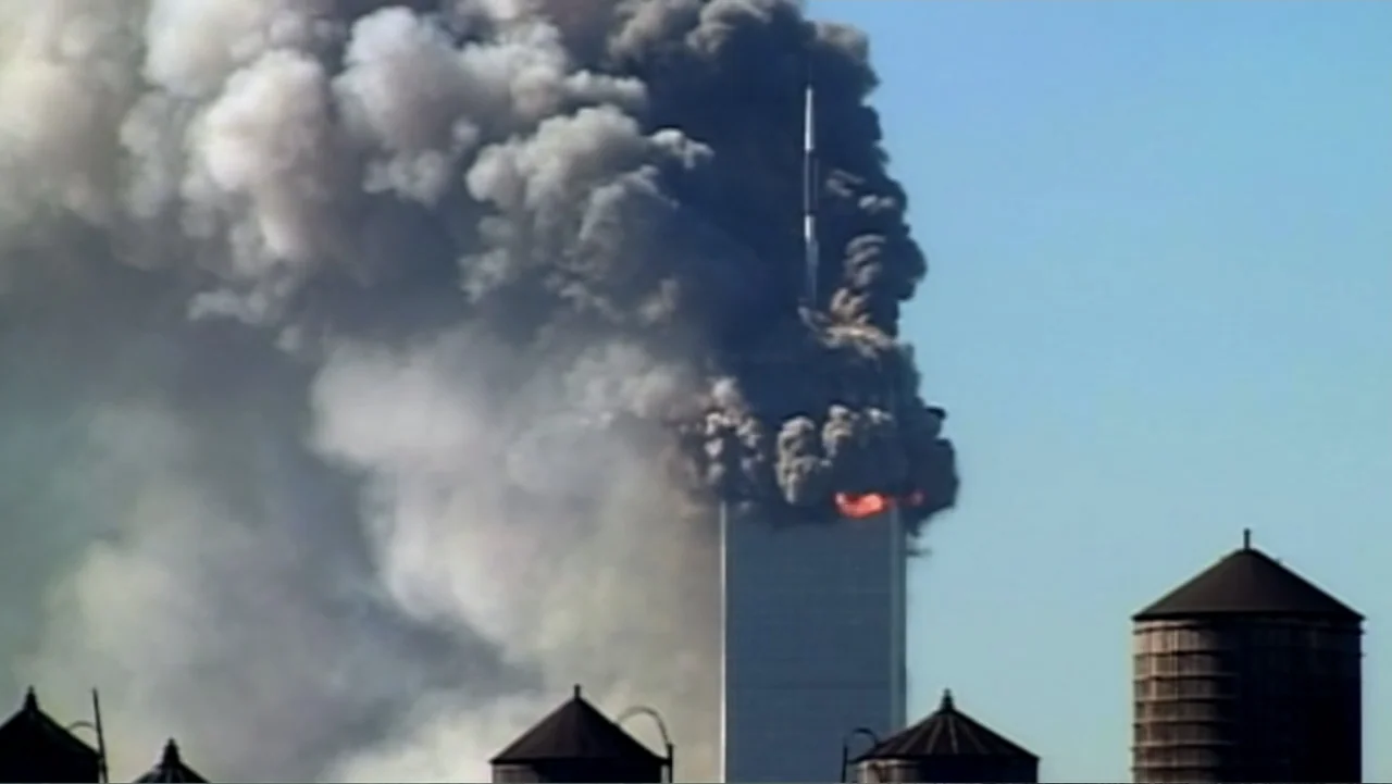 In the Shadow of the Towers: Stuyvesant High on 9/11 (2019) movie still: wide — A clear blue sky behind a tall skyscraper emitting a massive pillar…