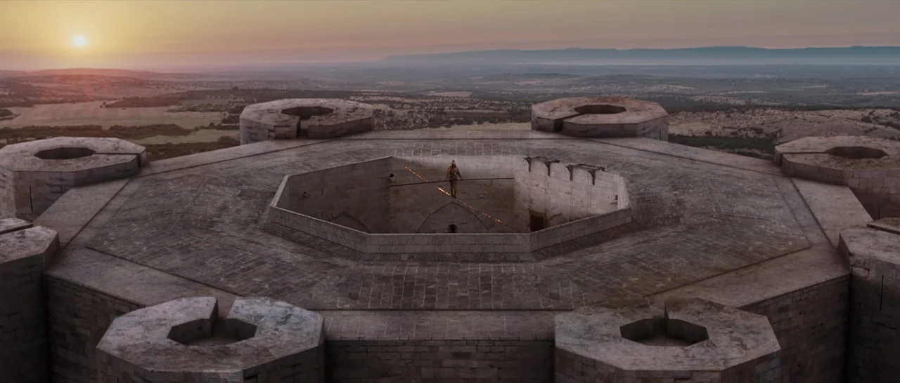 Tale of Tales (2015) movie still: wide — An octagonal stone castle roof overlooks a vast, flat landscape at golden hour. A single person carefully…