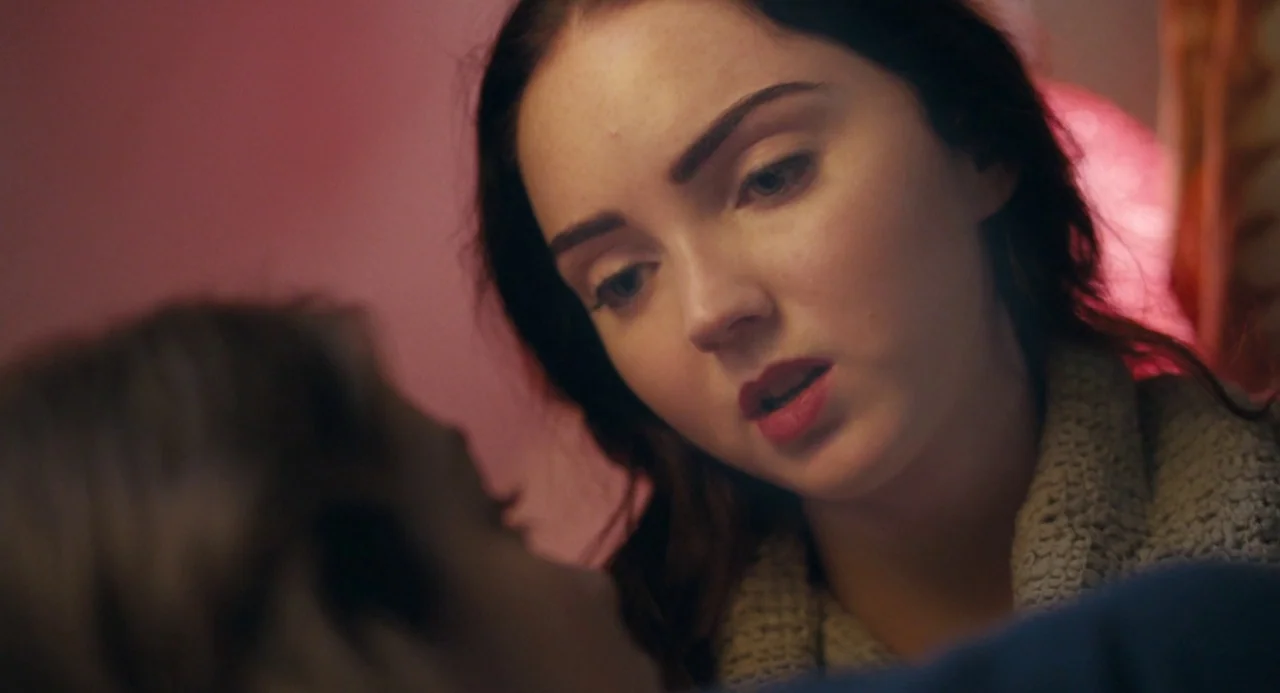 The Moth Diaries (2011) movie still: closeup — A dark bedroom interior with a warm pink light source casting a glow. A woman with dark hair leans…