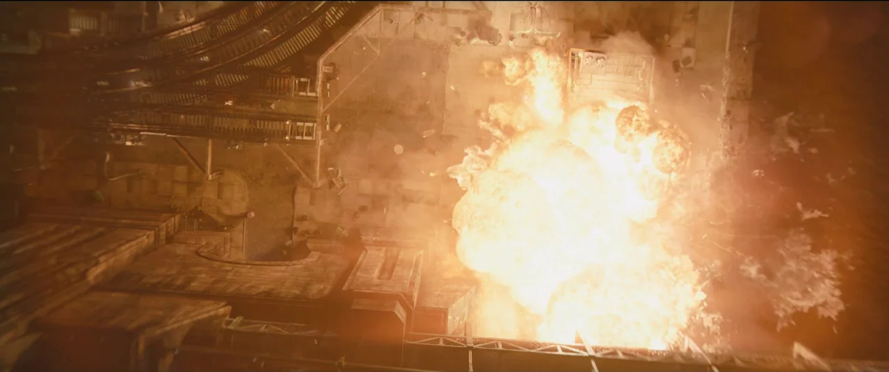 The Batman (2022) movie still: wide — An aerial view looks down upon a city street with elevated train tracks. A massive fireball consumes the space…