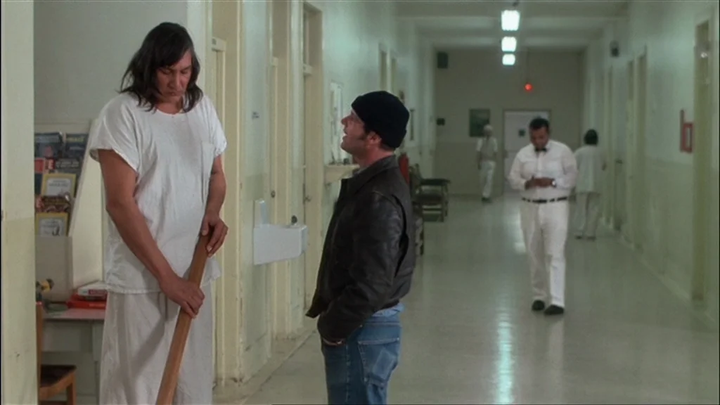 One Flew Over the Cuckoo's Nest (1975) movie still: fullbody — A long institutional hallway with pale walls and beige doors stretches into the…