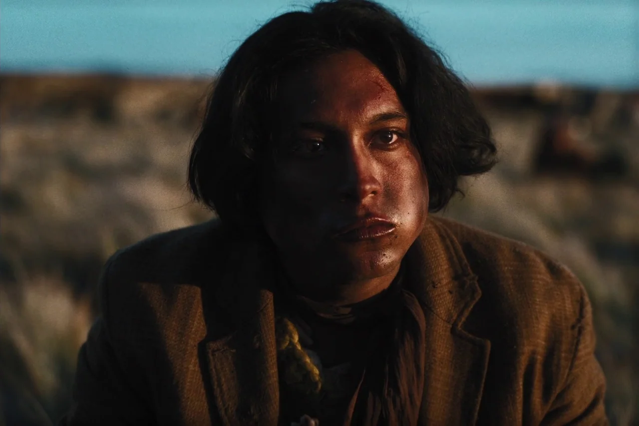 The Settlers (2023) movie still: closeup — A man stands in an open landscape during the warm glow of late day. The subject looks directly ahead…