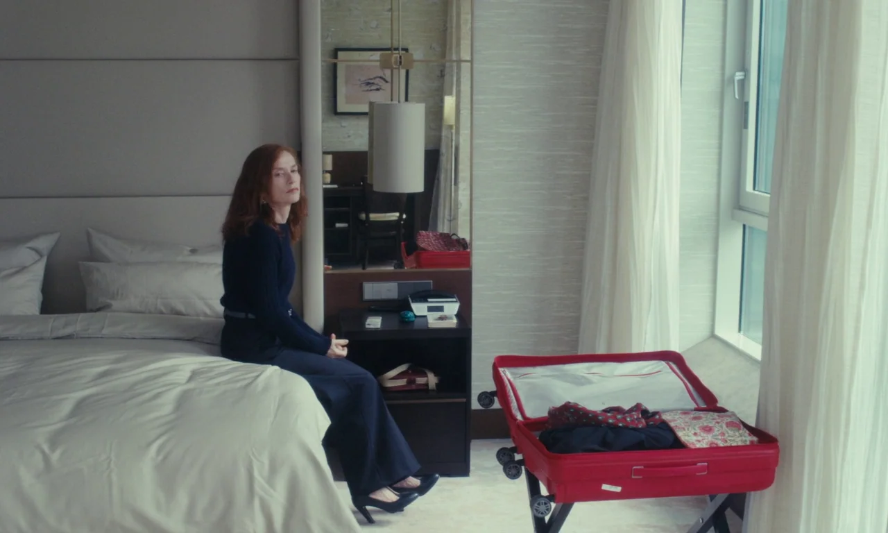 Sidonie in Japan (2023) movie still: medium — A modern hotel room features a bed, a bedside table, and a large window. A woman with reddish hair…