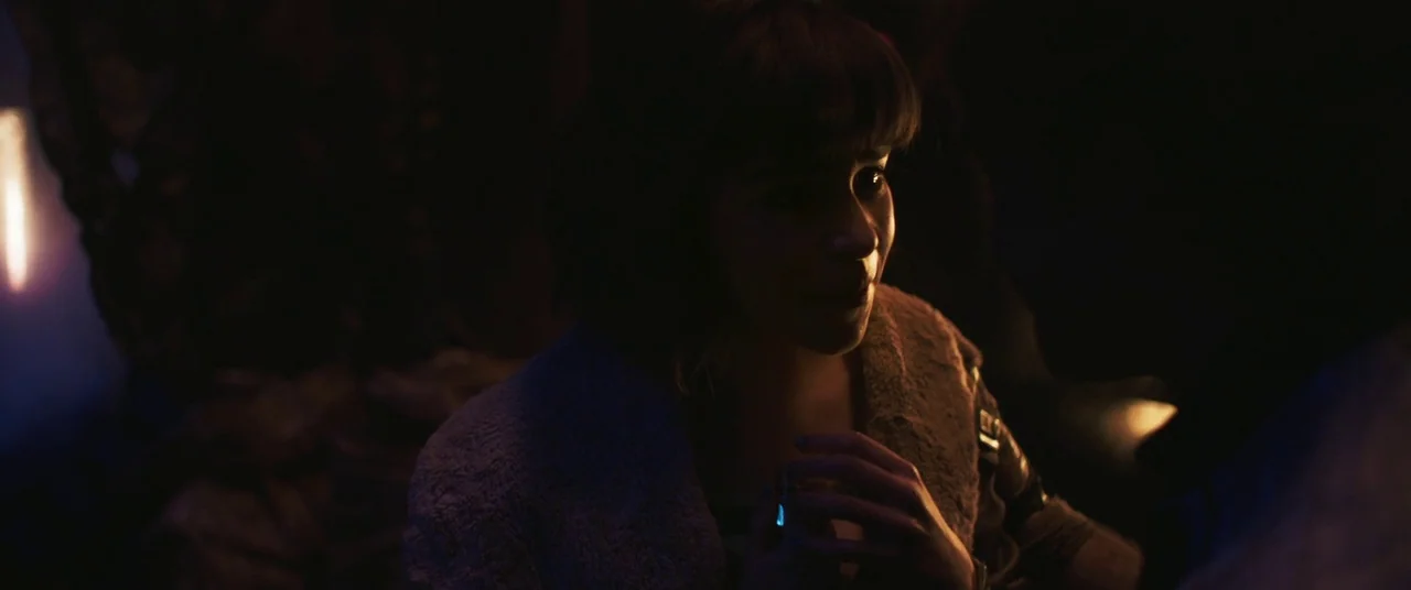 Solo: A Star Wars Story (2018) movie still: medium — A dimly lit interior space contains a woman in a textured, light-colored jacket. She holds a…